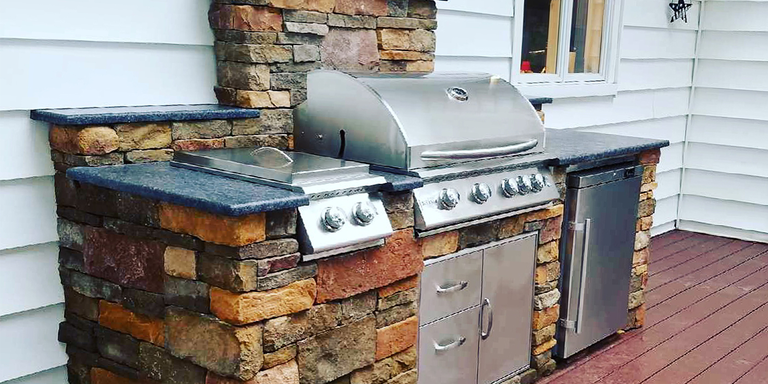 A small ready to finish outdoor kitchen island with a grill, cabinets, and a refrigerator