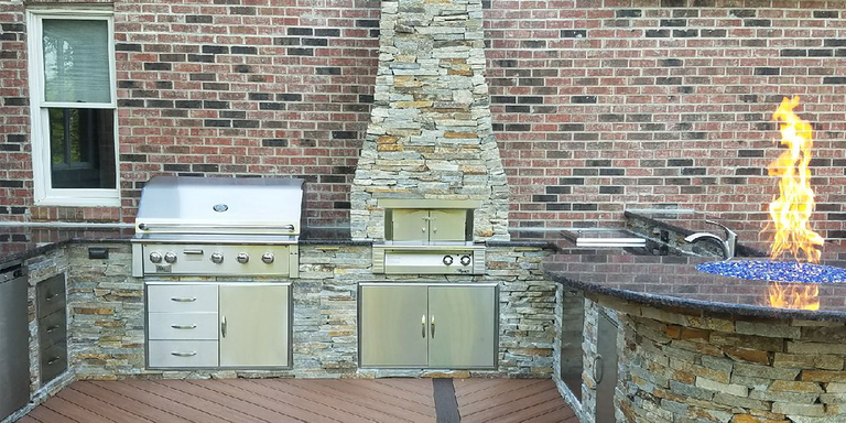 A custom-built outdoor kitchen island with a grill, storage doors, pizza oven, bar area, and fire pit