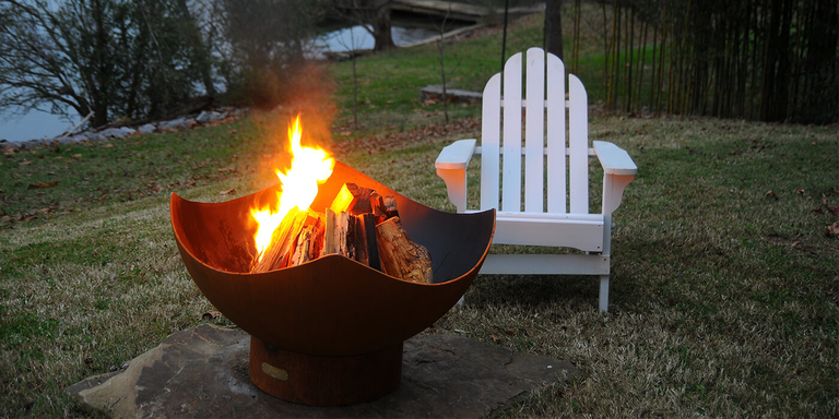 A backyard with a wood burning fire pit and chair set up on the lawn